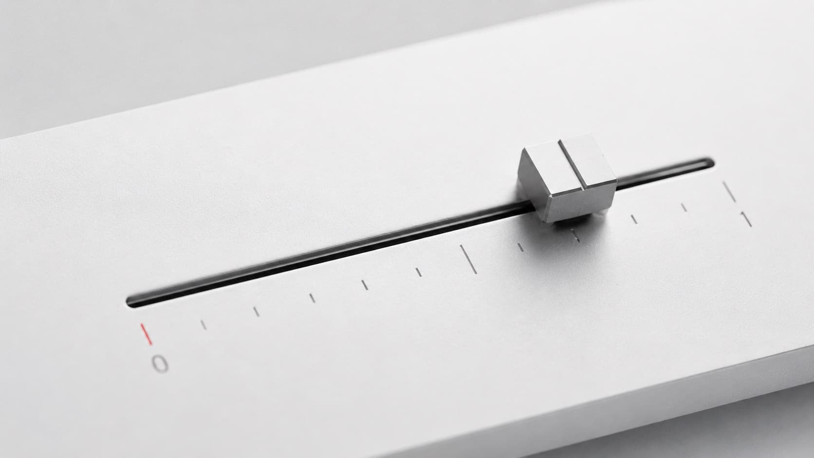 Physical slider fader on an aluminium panel with a fine engraved scale and a single red mark at zero